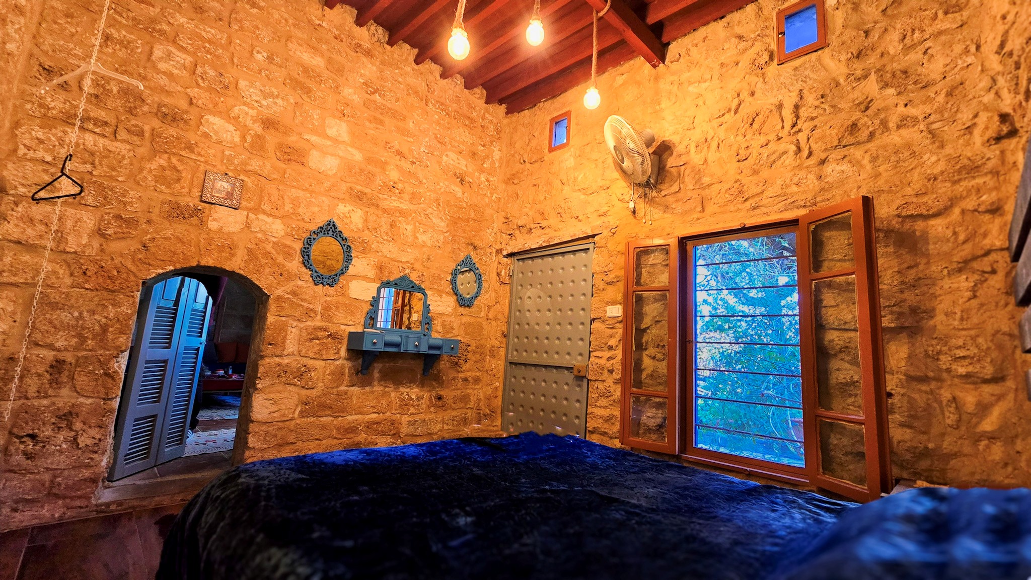 Spacious master bedroom at Beit Tout Guesthouse in Saida, featuring elegant wood furnishings and a stunning stone wall for a serene, unique atmosphere.